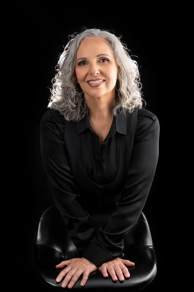 Rocío Pozo sonriendo, sentada con las manos sobre las rodillas, sobre fondo negro